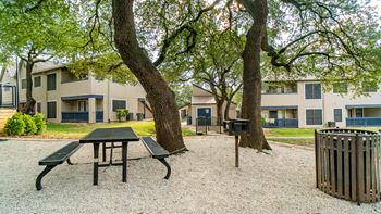 a park with a picnic table and a trash can in front of apartment buildings